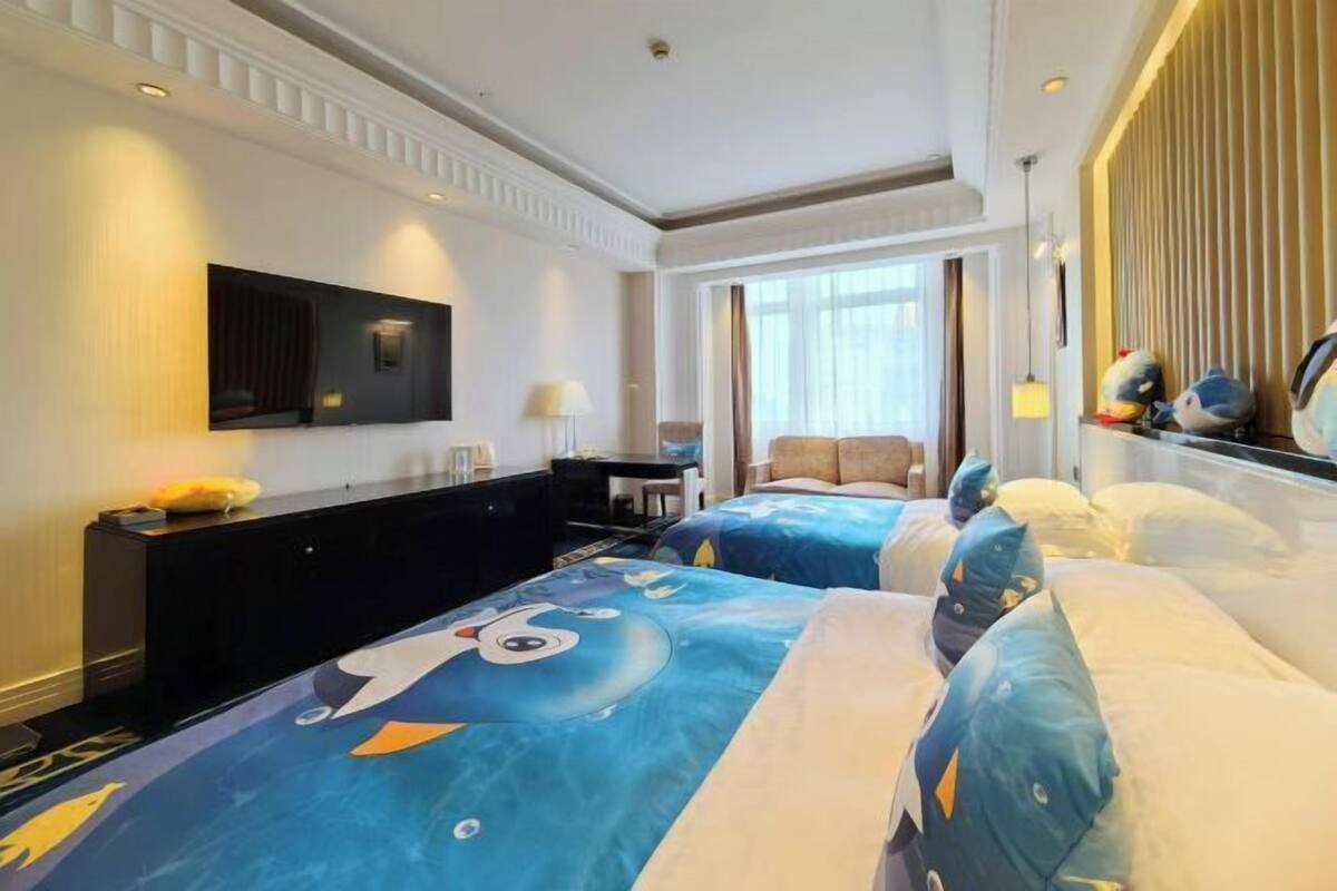 Quarto de hotel com duas camas, uma escrivaninha, uma cadeira, uma televisão e uma janela com cortinas.