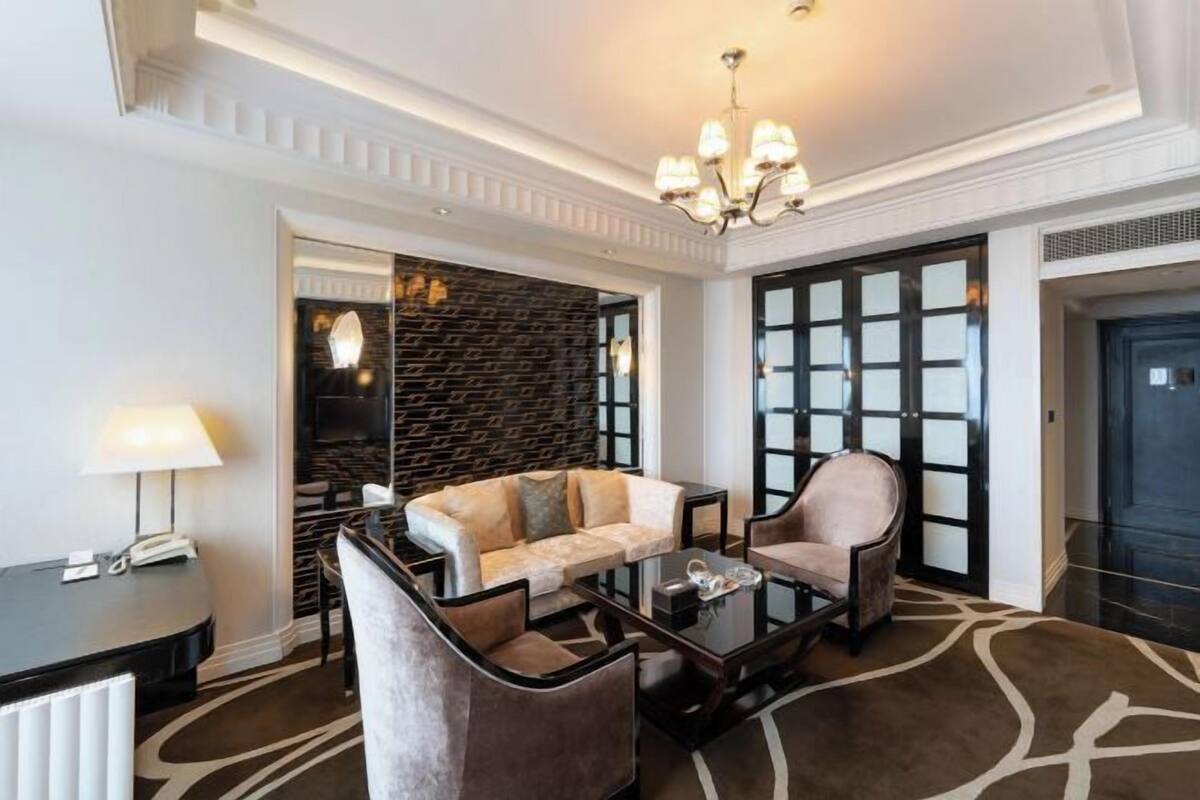 Um saguão de hotel com um sofá, poltronas, uma mesa de centro, uma luminária, um telefone e um tapete estampado.