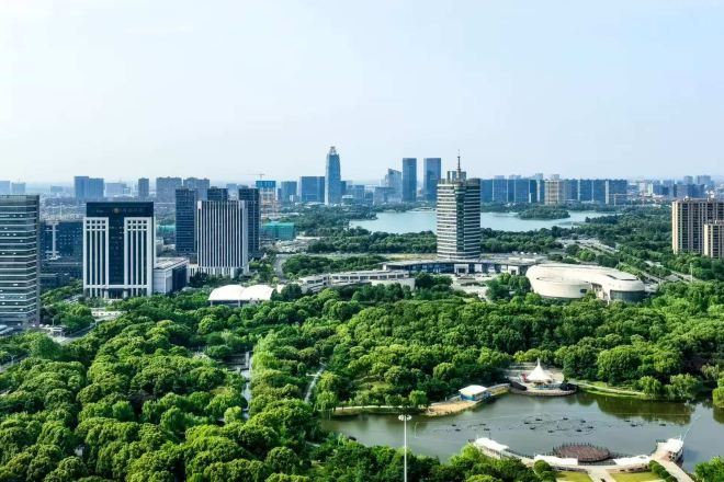 A cityscape with modern high-rise buildings, a large green park area, and a body of water with a fountain.