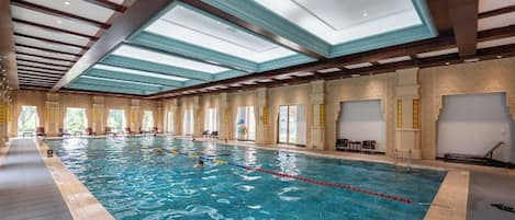 An indoor swimming pool with clear water, a diving board, and a ceiling with skylights.