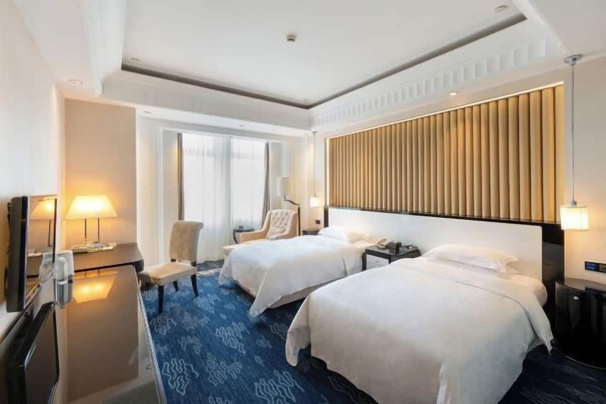 Quarto de hotel com duas camas, uma escrivaninha, uma cadeira e uma televisão.