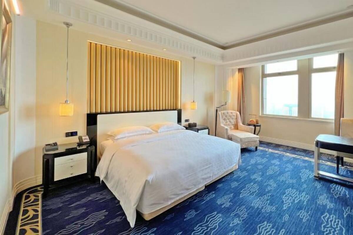 Quarto de hotel com uma cama grande, uma escrivaninha, uma cadeira e uma janela com vista.