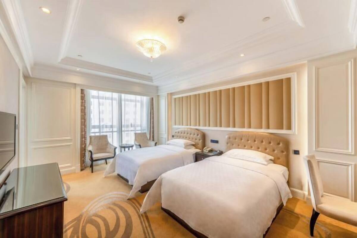 Quarto de hotel com duas camas, televisão, secretária e uma cadeira.