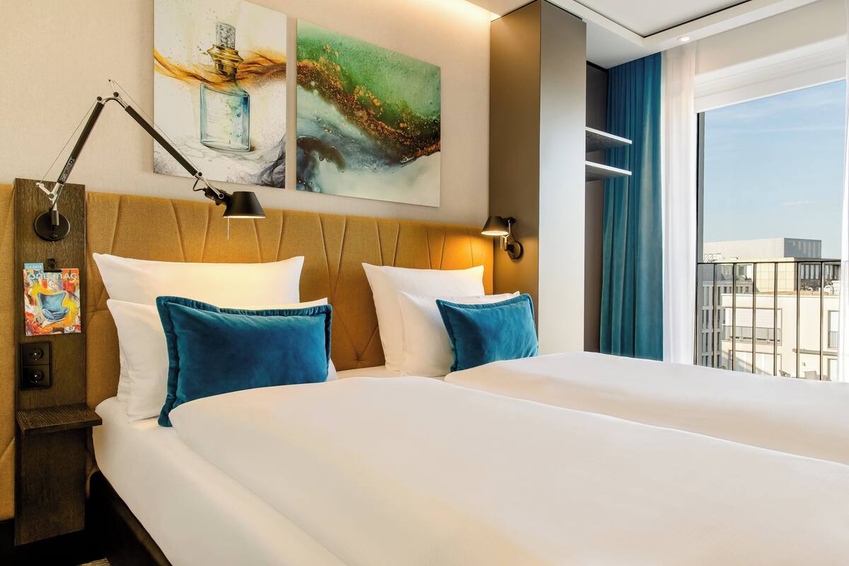 Une chambre d’hôtel avec un grand lit, deux tables de chevet, une lampe fixée au mur et des œuvres d’art.