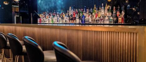 A bar area with a row of stools and a wall of liquor bottles.