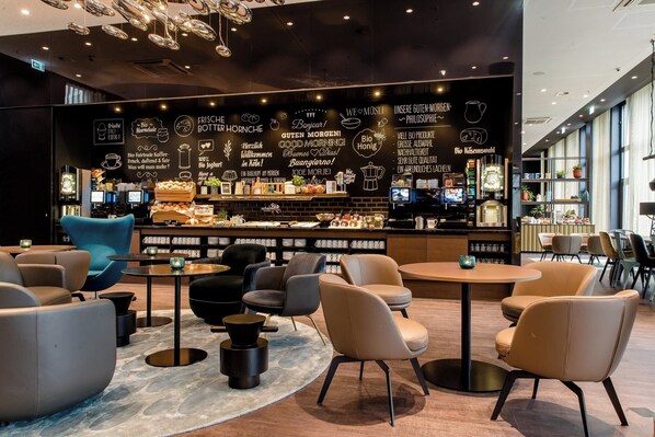 Un café moderno con pared negra con texto y gráficos blancos, asientos cómodos y una barra con diversos artículos a la vista.
