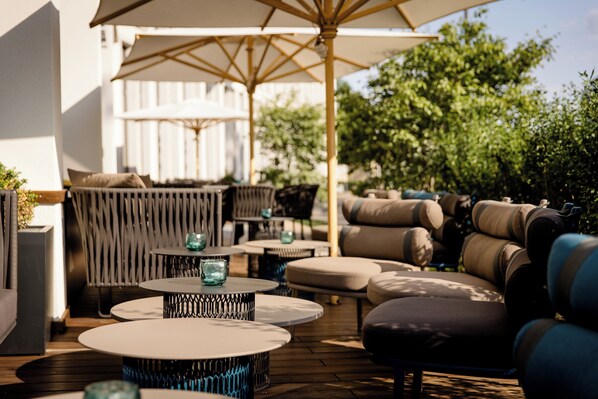 Un espace extérieur aménagé avec des tables rondes, des canapés confortables et des parasols.