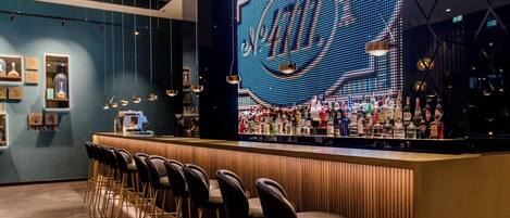 A bar area with a digital display, bar stools, and a variety of bottles.