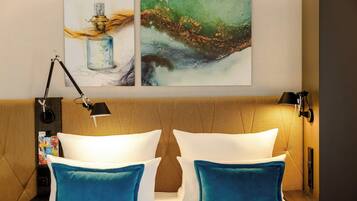 A hotel room with a bed, two pillows, a nightstand, a lamp, and two wall art pieces.