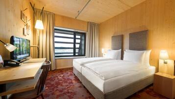 A hotel room with a wooden interior, a large bed, a desk with a computer, and a window with curtains.