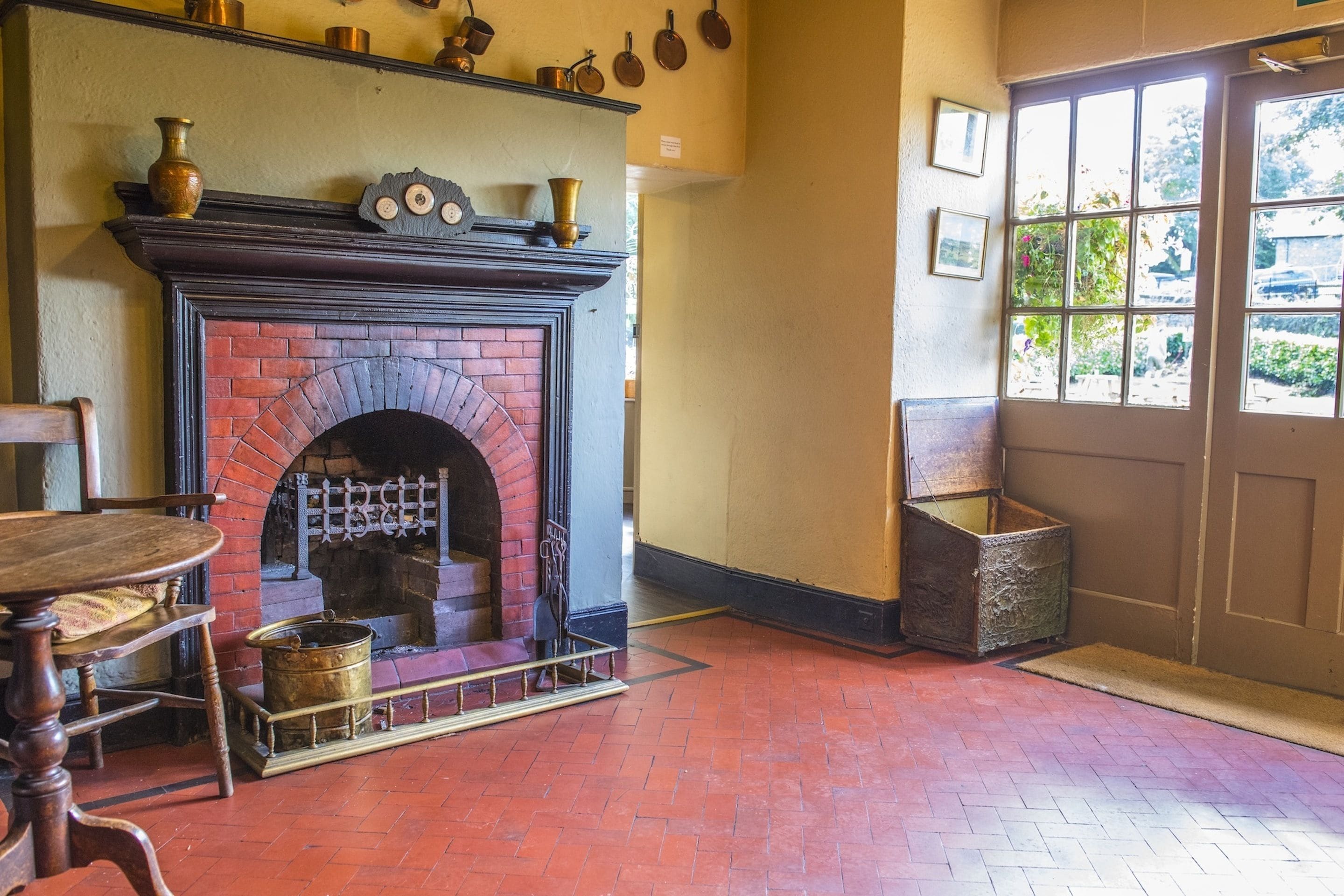 A room with a brick fireplace, a wooden table, and a door leading outside.