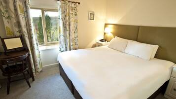 A hotel room with a large bed, a bedside table with a lamp, a chair, and a desk with a computer.