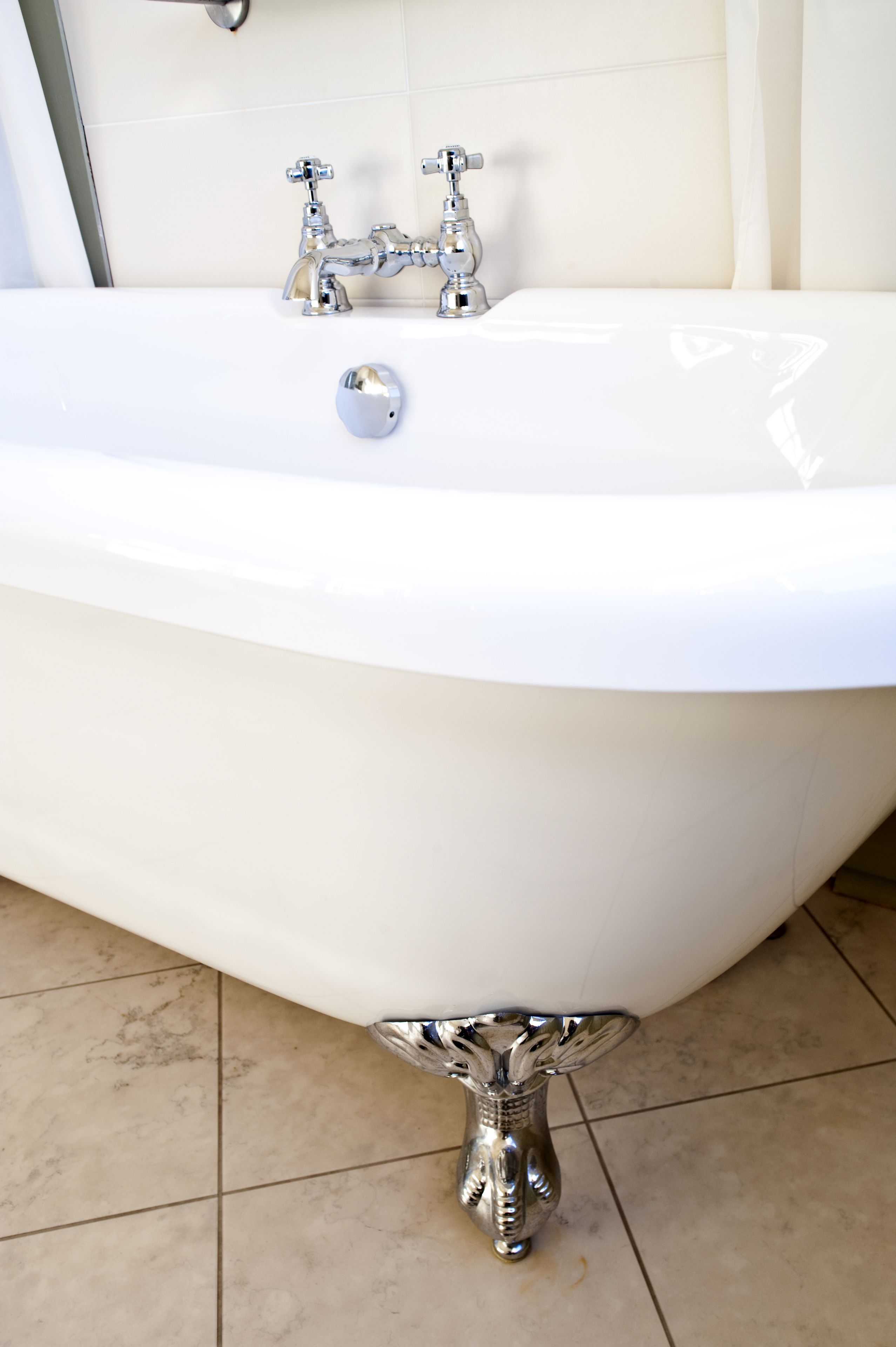 A white bathtub with chrome fixtures in a bathroom with tiled flooring.