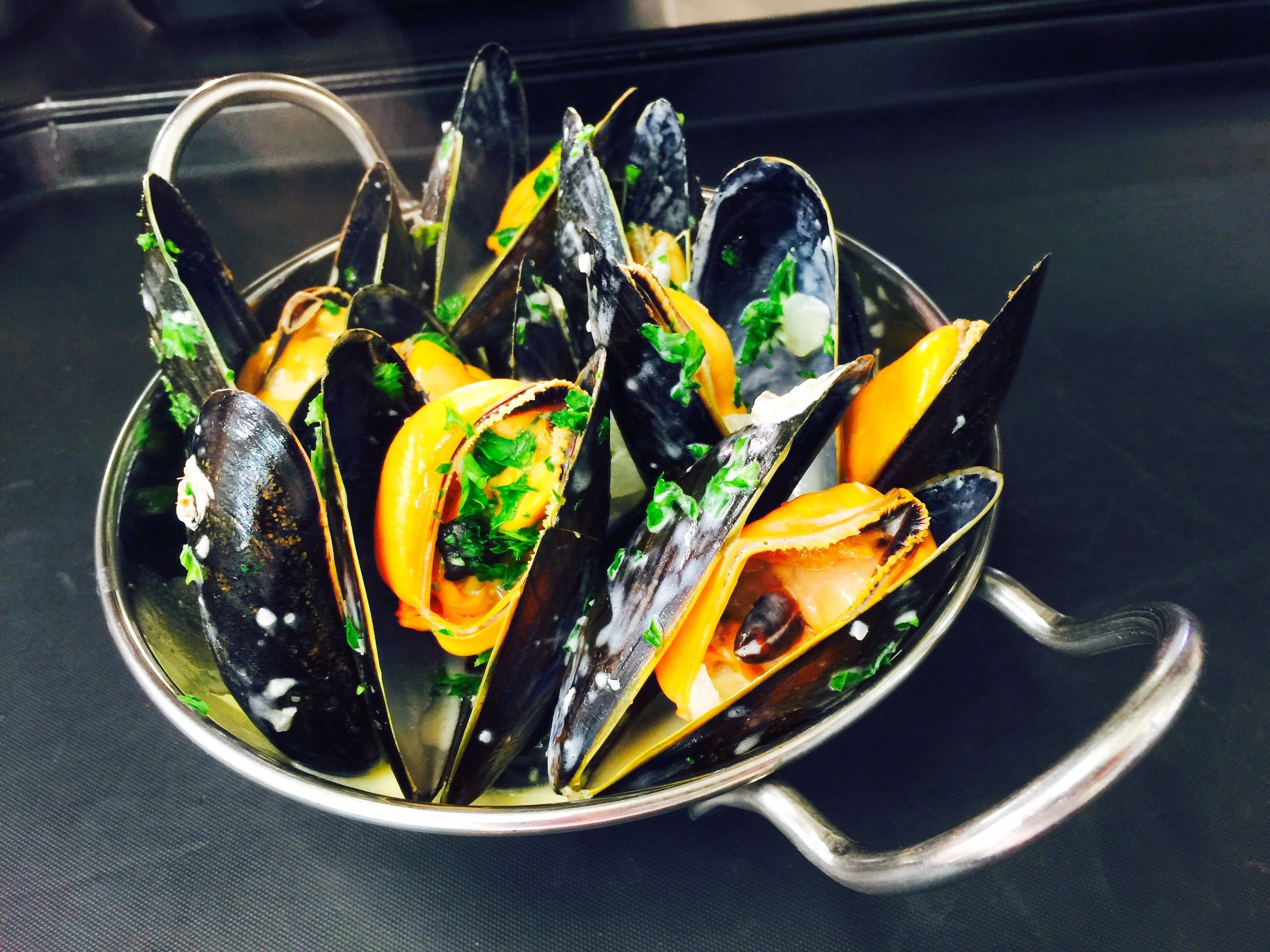 A bowl of mussels with herbs and lemon slices.