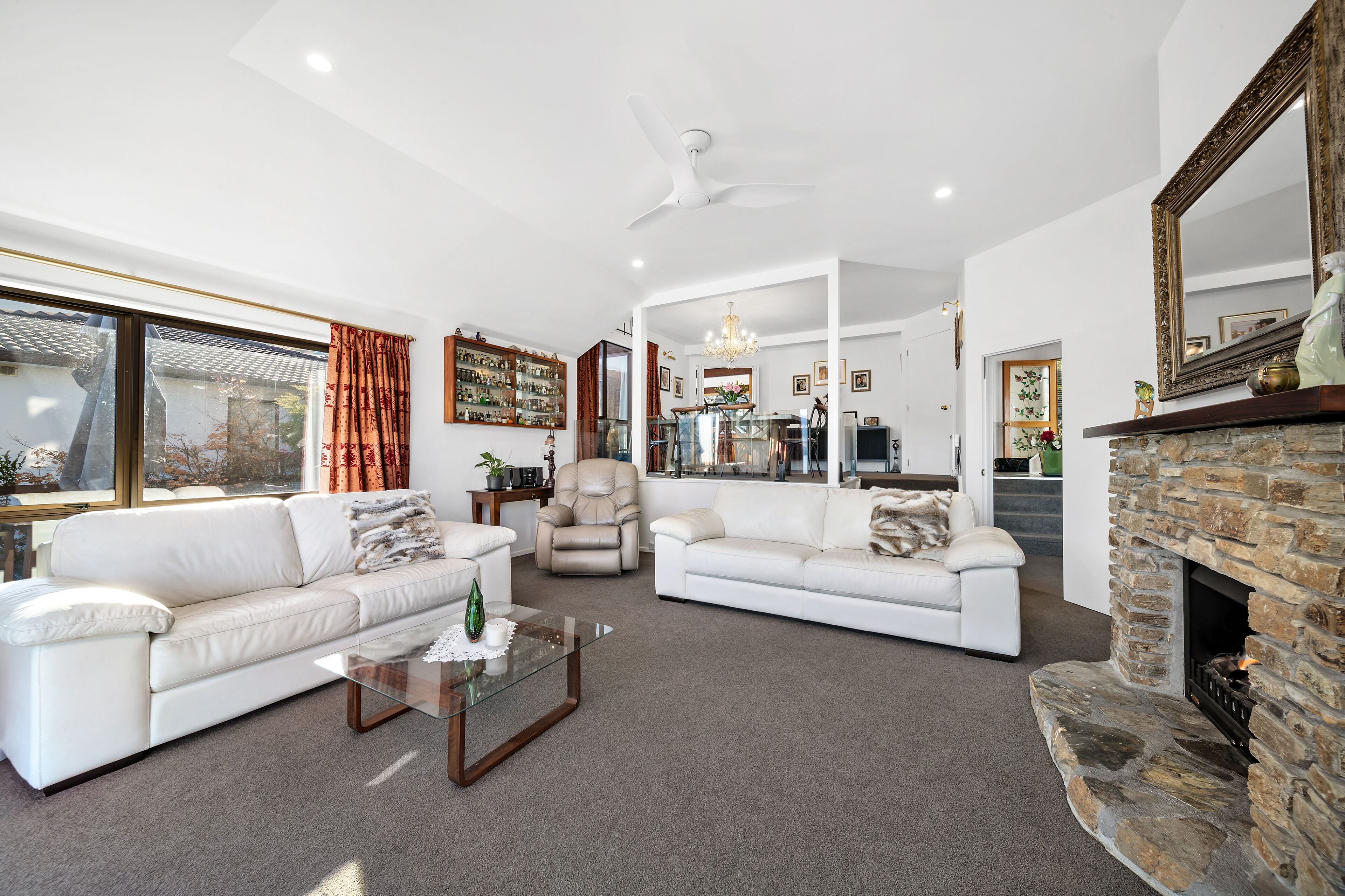 A spacious living room with a white sofa, a glass coffee table, and a stone fireplace.