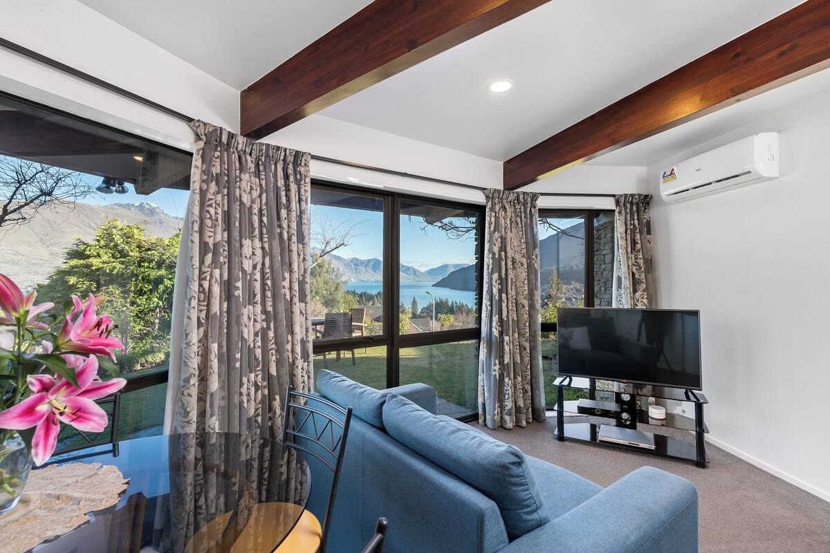 A modern living room with a large window, a flat-screen TV, and a blue sofa.