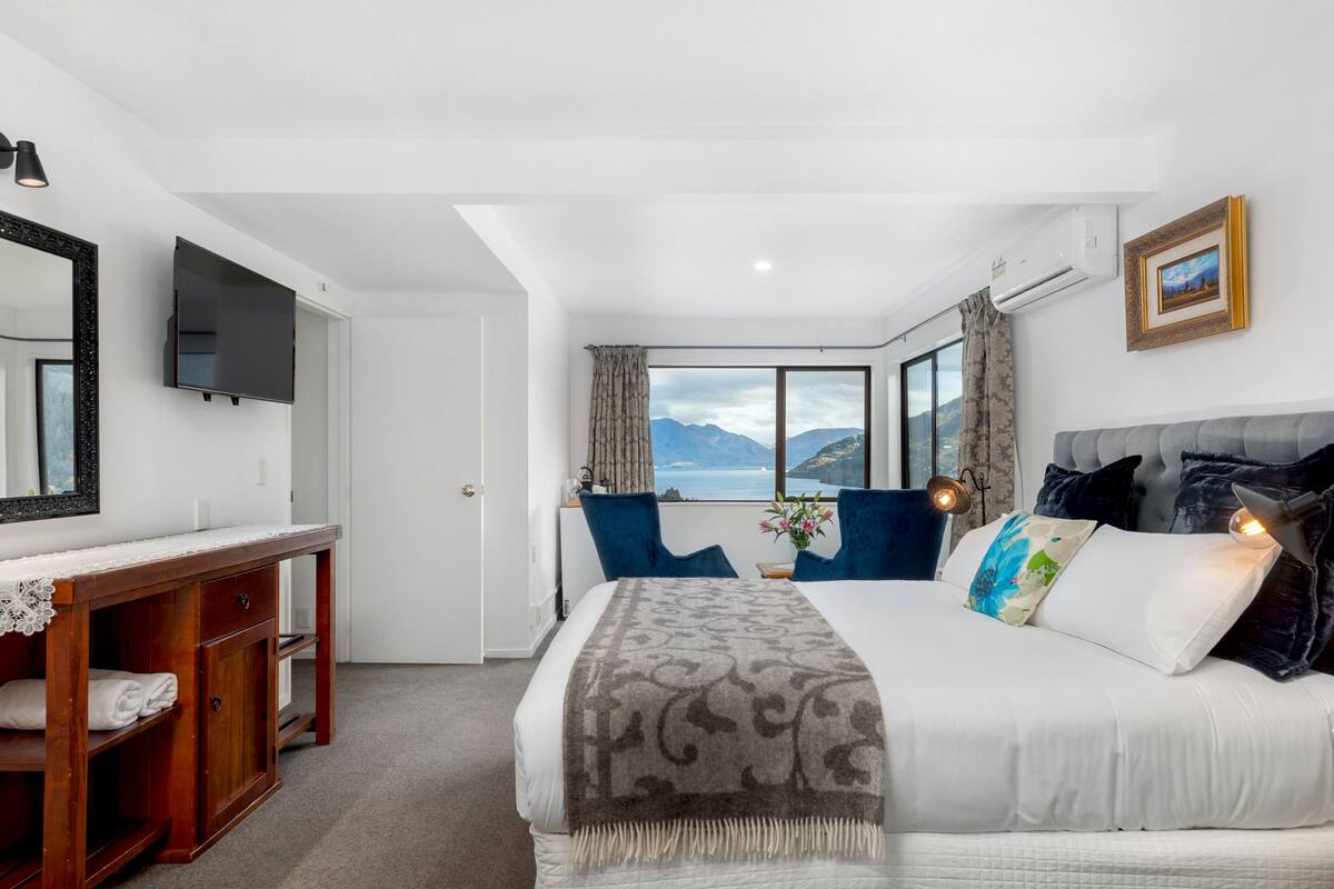 A hotel room with a bed, a desk, a TV, and a window with a mountain view.