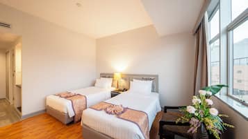 A hotel room with two beds, a nightstand, a desk, and a window with a view of buildings.