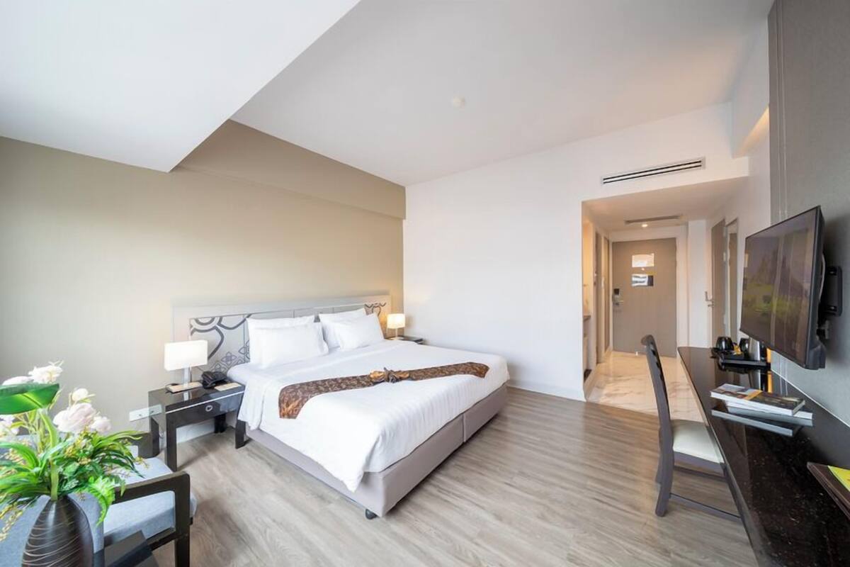 A modern hotel room with a large bed, bedside tables, a desk, and a flat-screen TV.