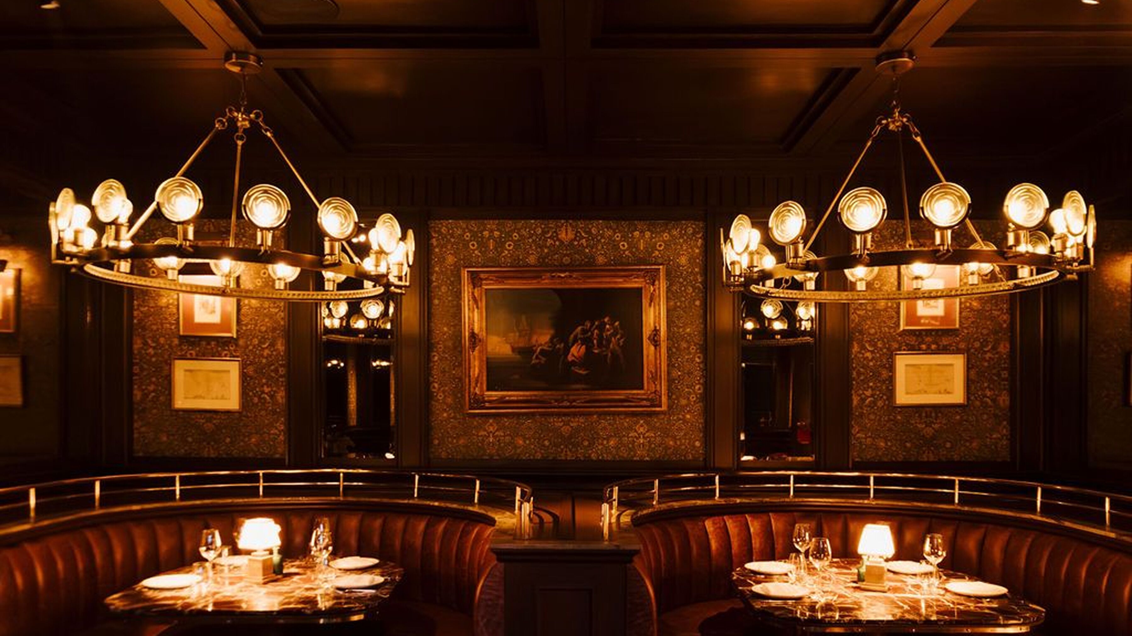 A dimly lit restaurant with ornate chandeliers, a central painting, and leather booths.