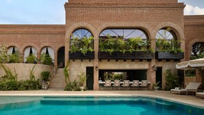 Un área junto a la piscina con un edificio de ladrillo, mobiliario exterior y plantas.