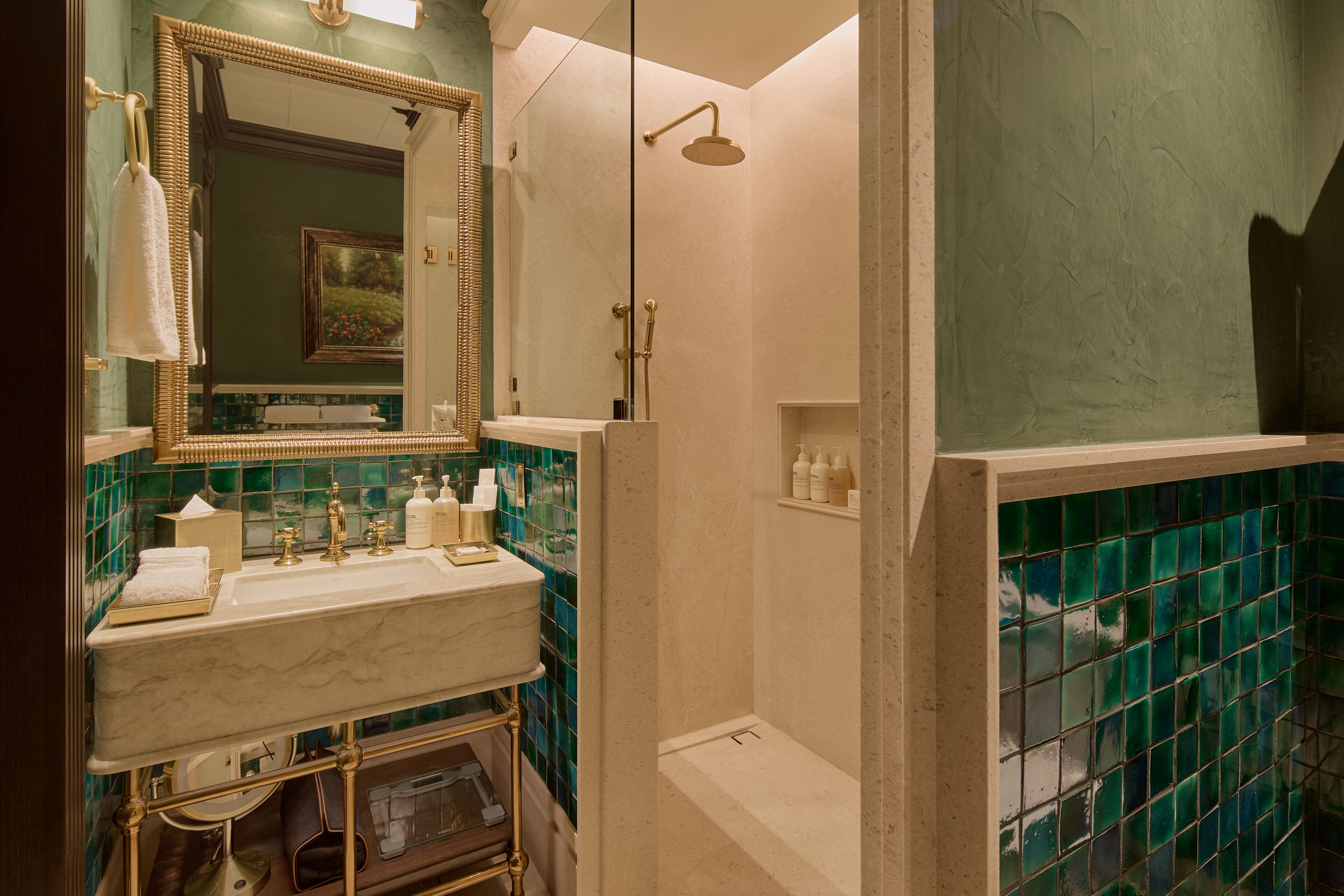 Un baño con lavamanos de mármol, un espejo con marco dorado y paredes con azulejos verdes.