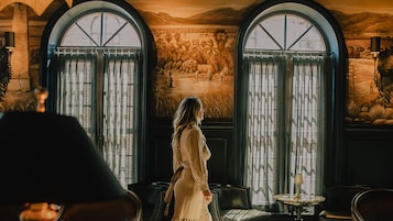 Una habitación con ventanales de arco, un mural y una persona de pie junto a las ventanas.