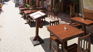 Un café al aire libre con mesas y sillas de madera, un letrero y un edificio con una fachada naranja llamativa.