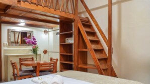 Un dormitorio con una cama litera de madera, un escritorio de madera con un espejo, una silla, una mesita con un florero y un juego de toallas sobre la cama.