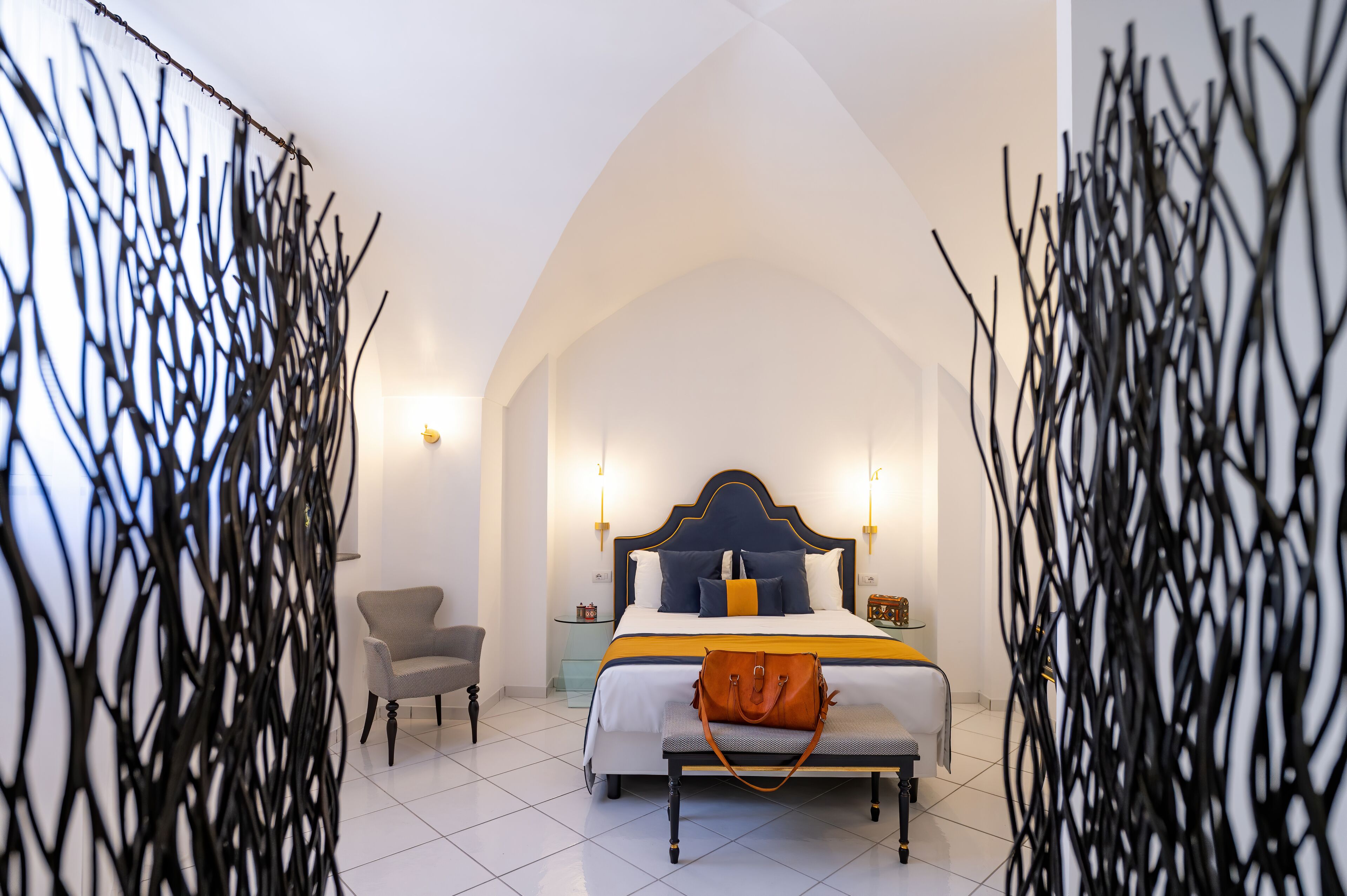 Un dormitorio con cama, mesitas de noche, una silla y decoración en la pared.