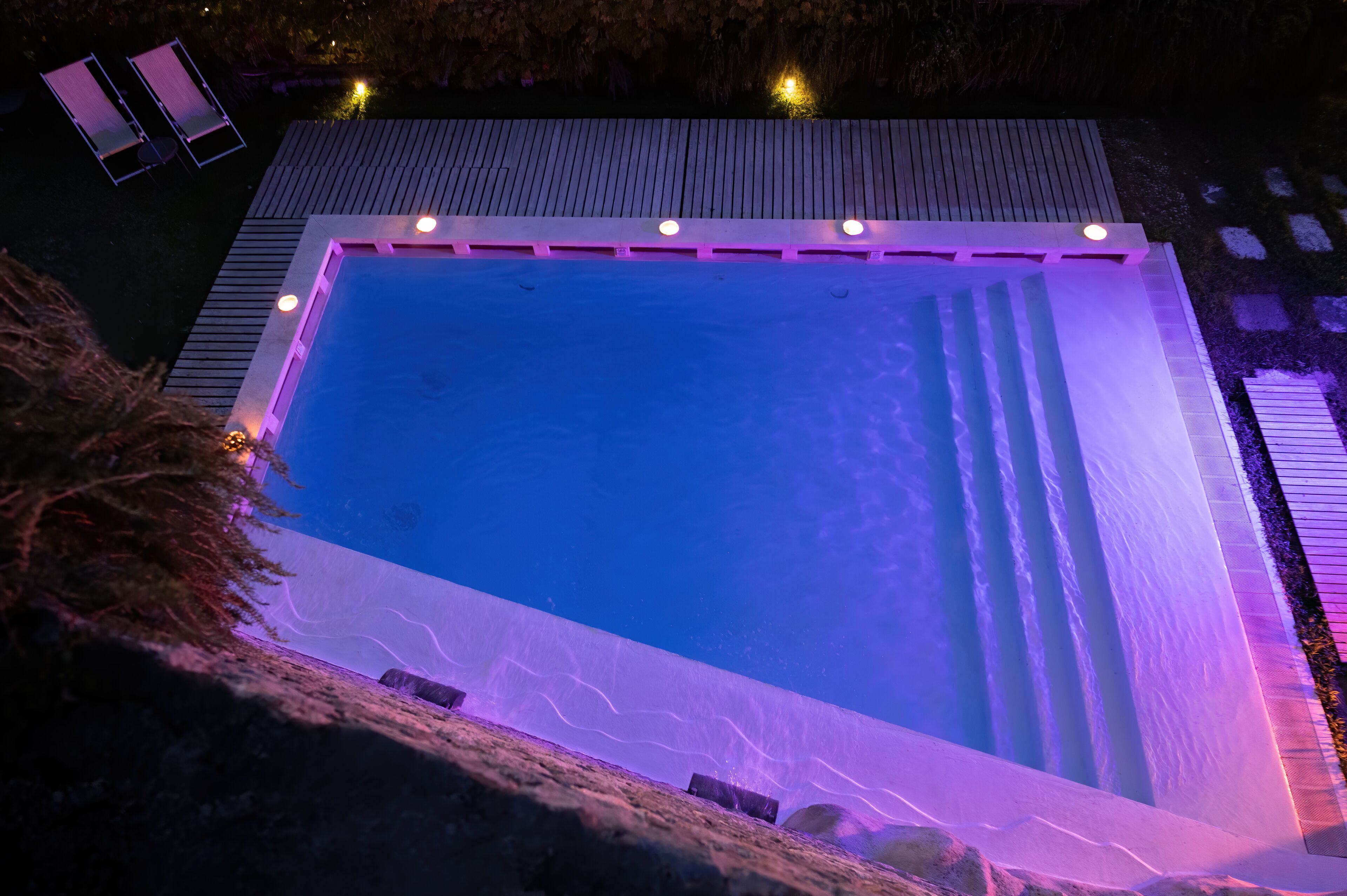 Ein rechteckiger Pool mit Holzterrasse und einer kleinen Sitzecke mit zwei Stühlen.