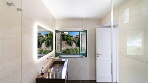 Un baño moderno con un espejo grande, un lavabo y una puerta que da a un balcón con vistas a zonas verdes y edificios.