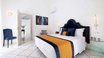 A modern hotel room with a large bed, a chair, a glass table, and a painting on the wall.