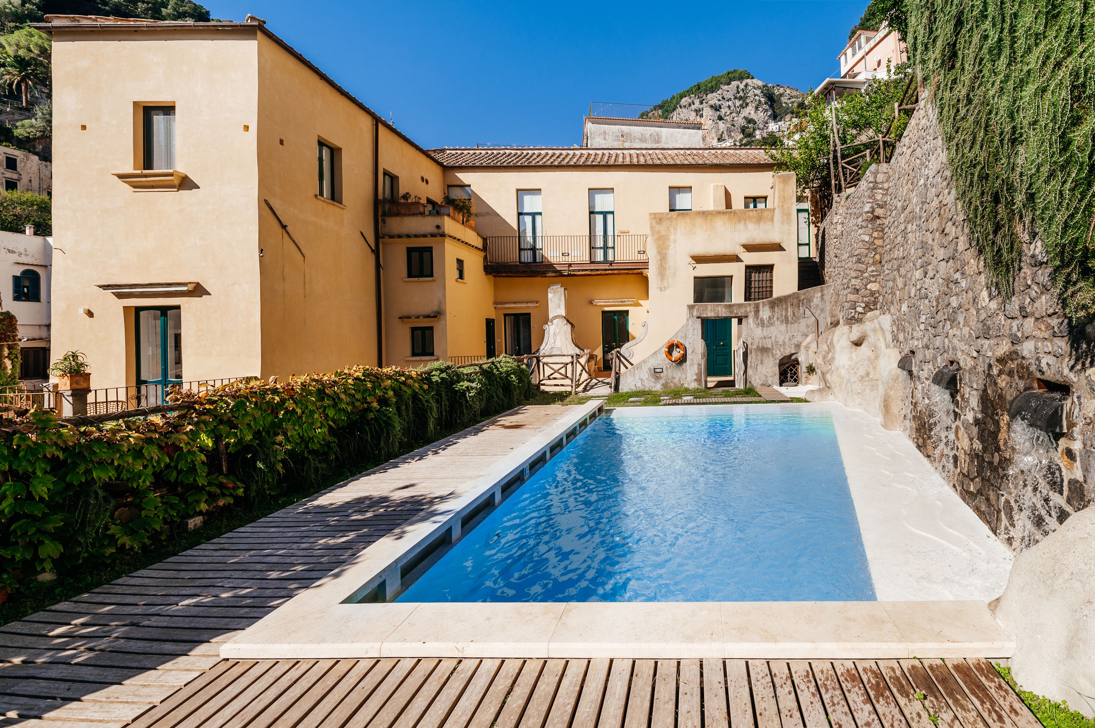 Una piscina con cubierta de madera, rodeada de edificios con balcones y un muro de piedra.