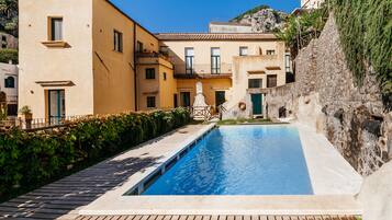 Una piscina con cubierta de madera, rodeada de edificios con balcones y un muro de piedra.