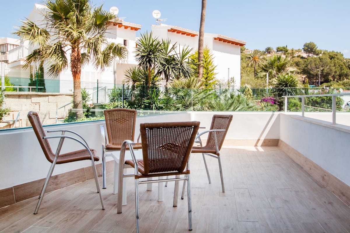 Une terrasse dotée de chaises en osier, offrant une vue sur un bâtiment blanc agrémenté de touches de rouge, le tout entouré de verdure.