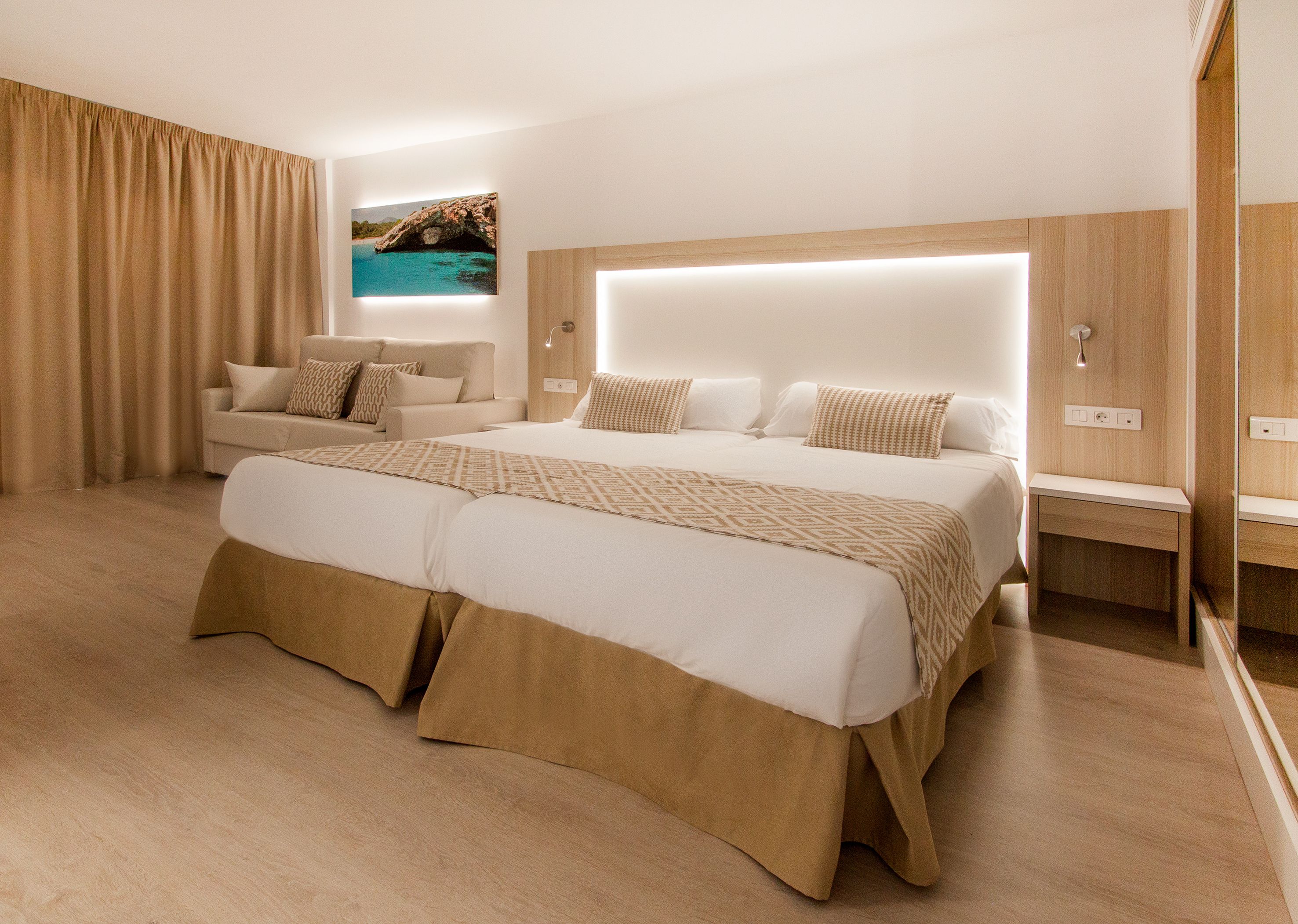 Una habitación de hotel moderna con una cama grande, un sofá, una mesita de noche y vistas al mar.