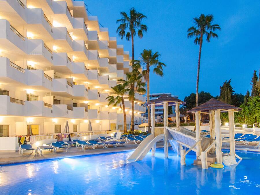 Zona de piscina de hotel con tobogán de agua, sillas de descanso y palmeras.