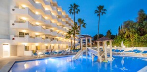 Un espace piscine d’hôtel avec un toboggan aquatique, des chaises longues et des palmiers.