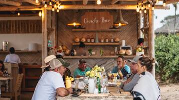 Un área de comedor al aire libre de estilo rústico, con mesas de madera y luces colgantes, que dice "Ceviche Bar".