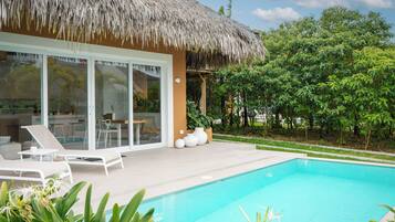 A modern villa with a pool, white lounge chairs, and a thatched roof structure.