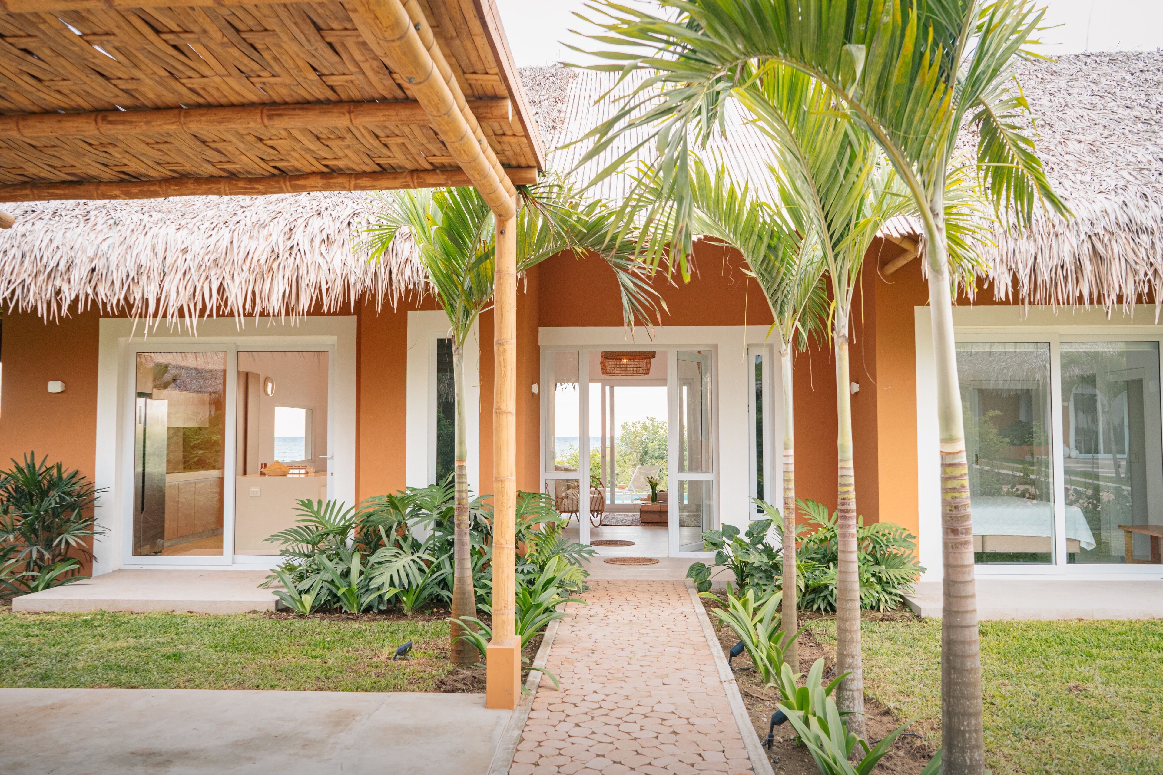 A resort with a thatched roof, palm trees, and a paved walkway leading to the entrance.