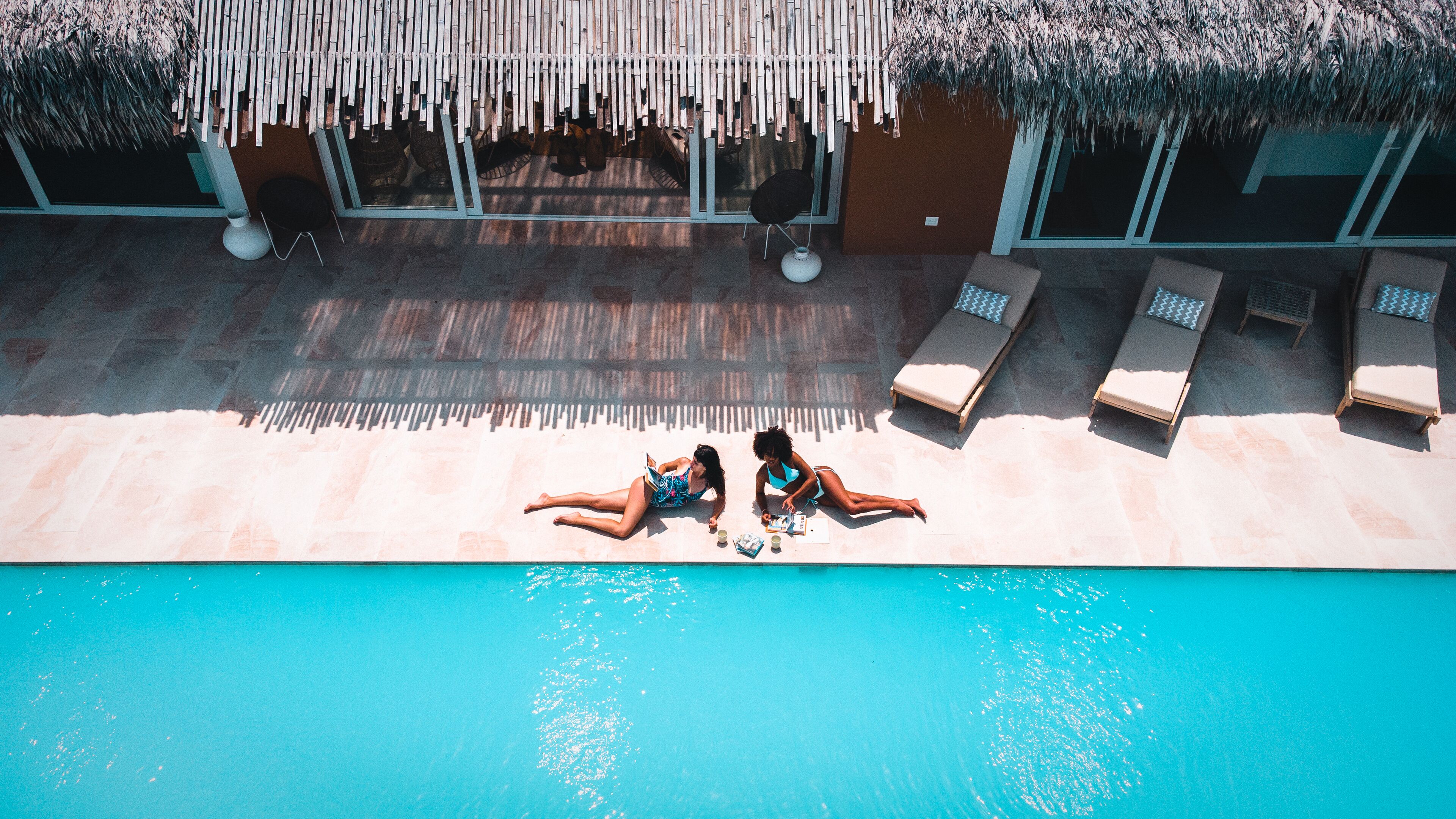 An aerial view of a swimming pool area with lounge chairs and a thatched roof structure.