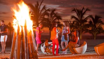 Un grupo de personas reunidas alrededor de una fogata en la playa al atardecer.