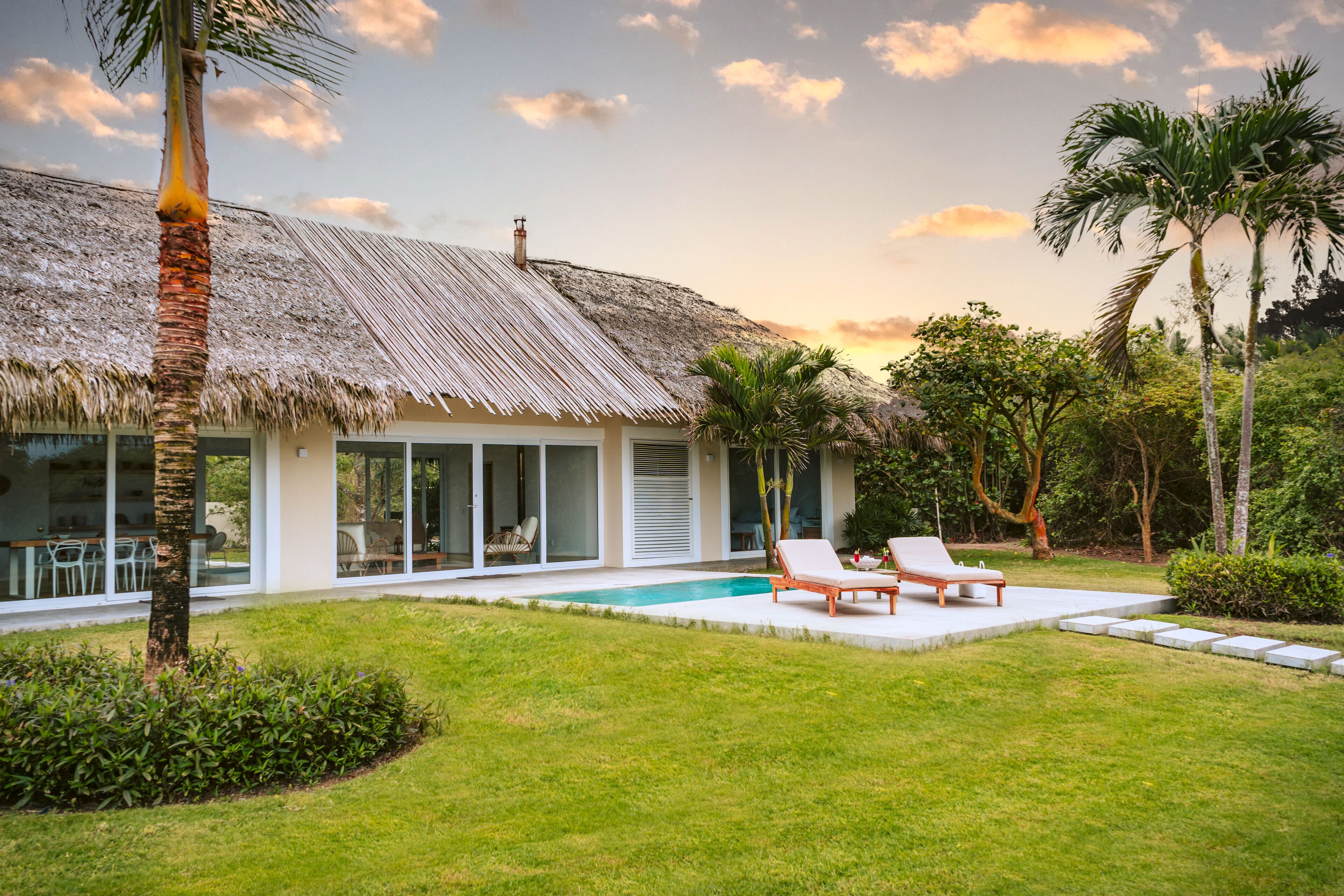 Ein modernes Haus mit Strohdach, Schwimmbad und einem gepflegten Garten.