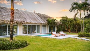 Ein modernes Haus mit Strohdach, Schwimmbad und einem gepflegten Garten.