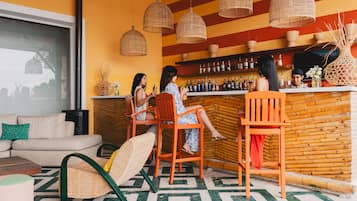 Un área de bar con sillas de mimbre y un sofá, una barra con botellas y un piso con diseño.