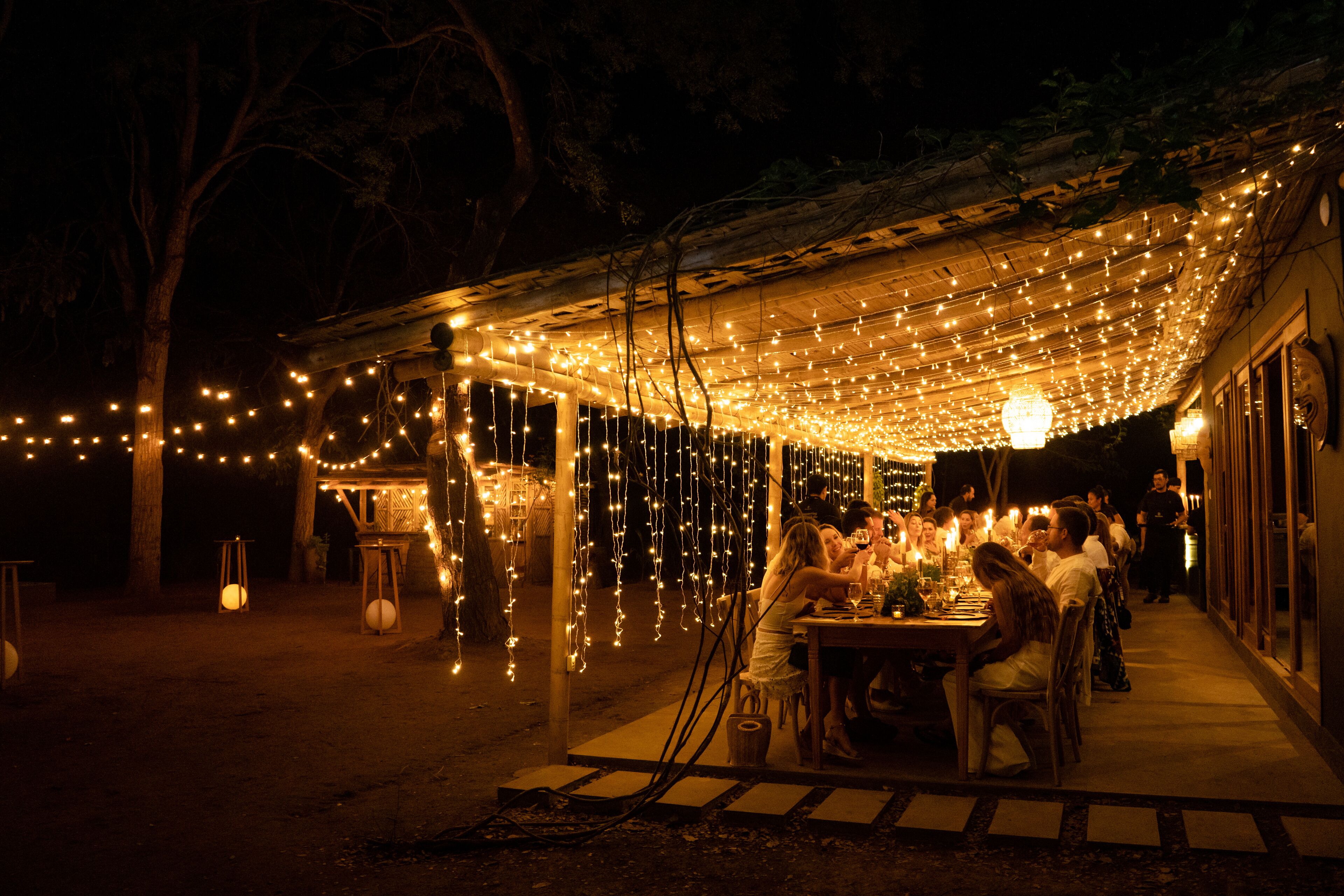 An outdoor dining area with string lights, wooden tables, and chairs.