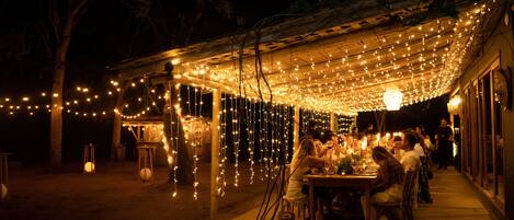 An outdoor dining area with string lights, wooden tables, and chairs.
