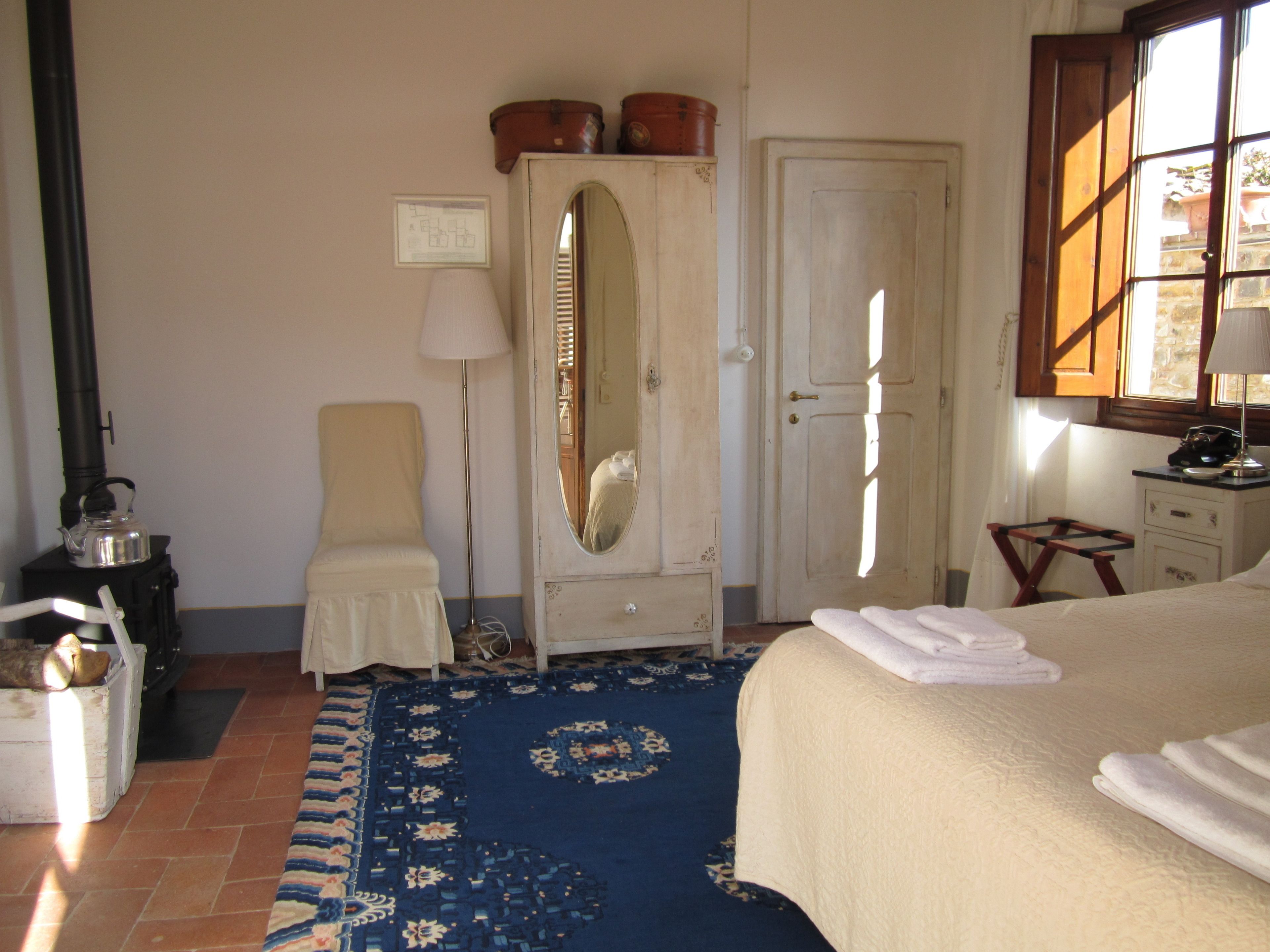 Un dormitorio con cama, cómoda, espejo, silla, lámpara y ventana.